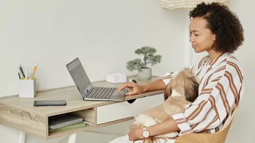 Persoon werkt aan laptop terwijl een hond op schoot ligt.